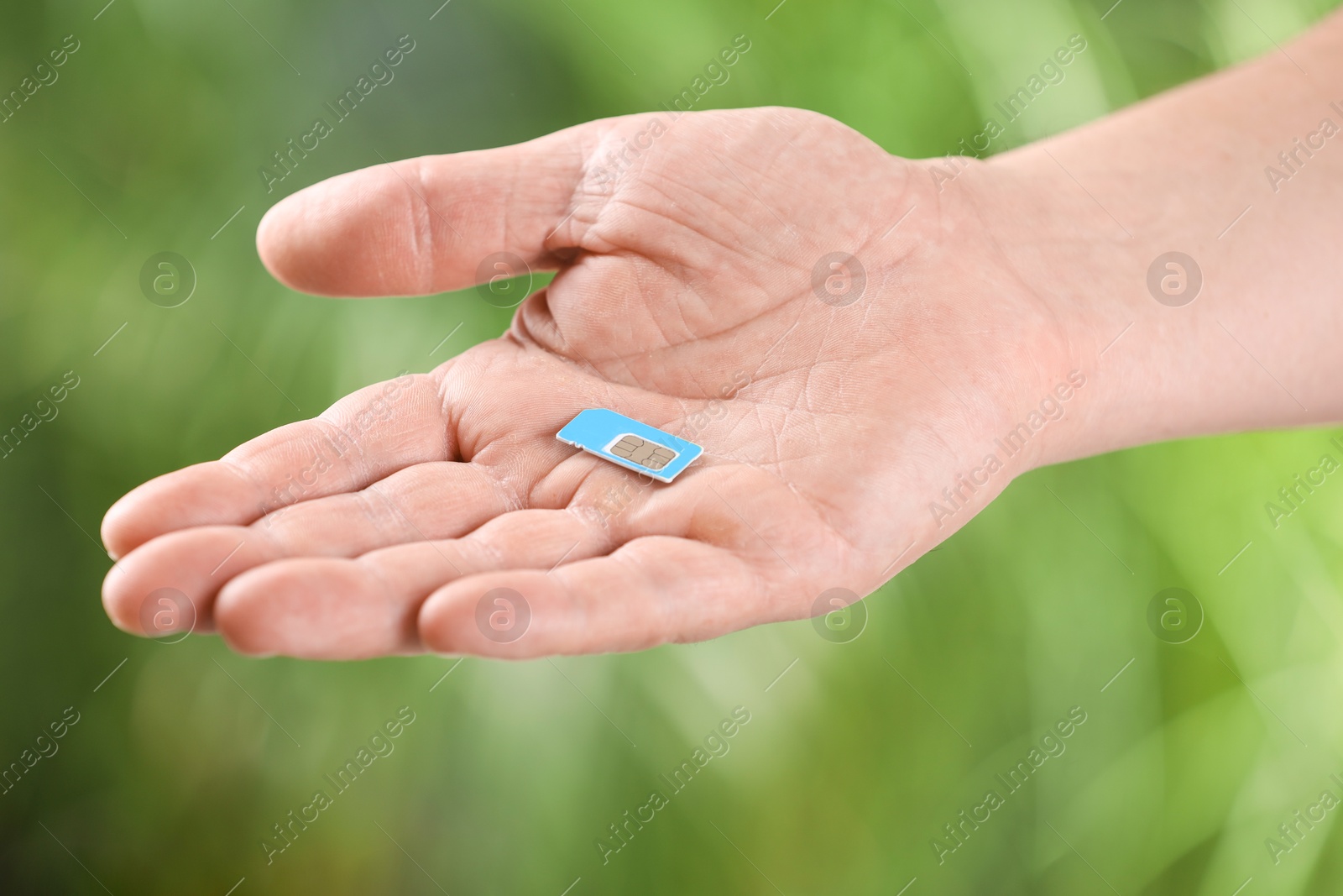 Photo of Woman with SIM card against blurred green background, closeup