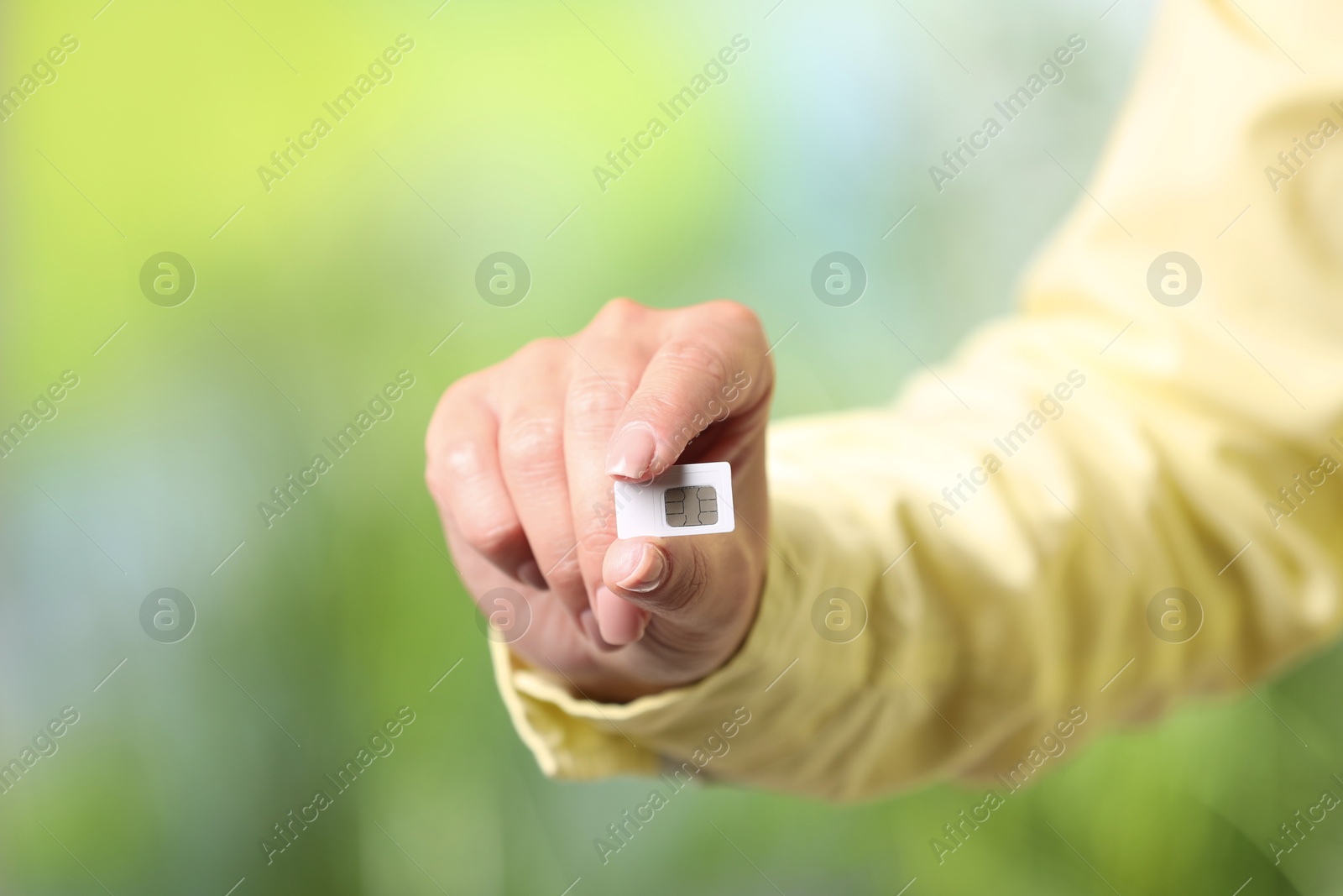 Photo of Woman with SIM card against blurred green background, closeup