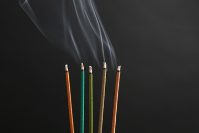 Photo of Aromatic incense sticks smoldering on black background