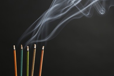 Photo of Aromatic incense sticks smoldering on black background