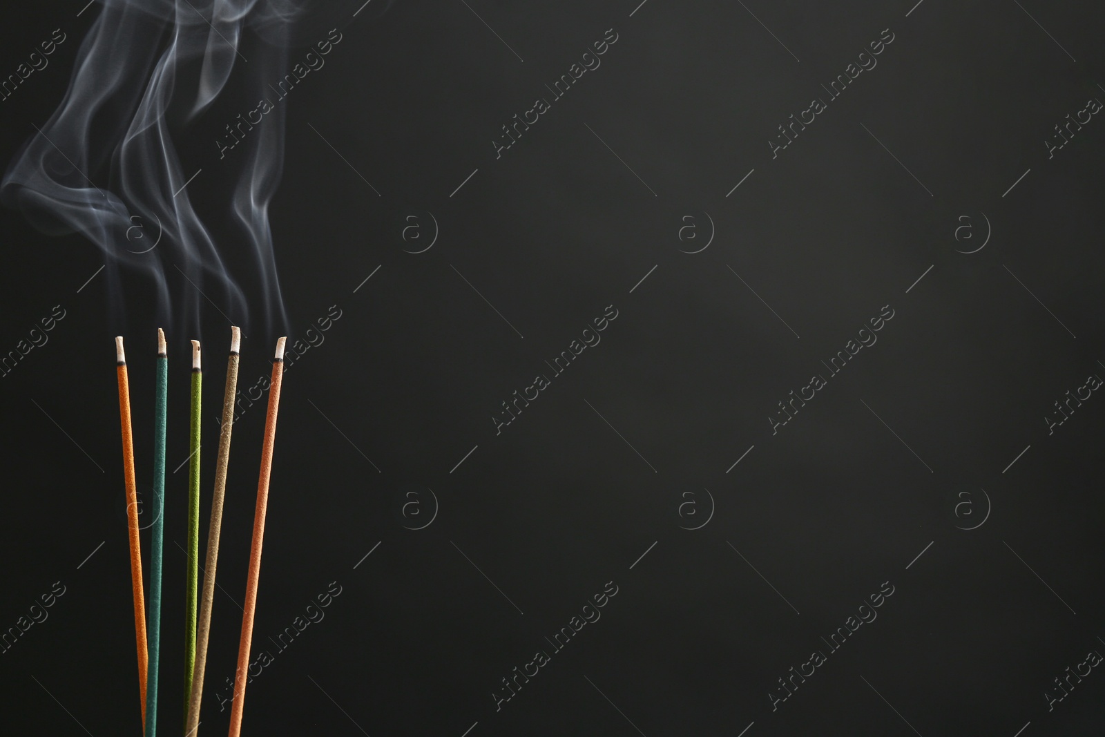 Photo of Aromatic incense sticks smoldering on black background. Space for text