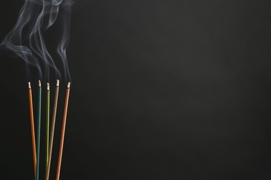 Photo of Aromatic incense sticks smoldering on black background. Space for text