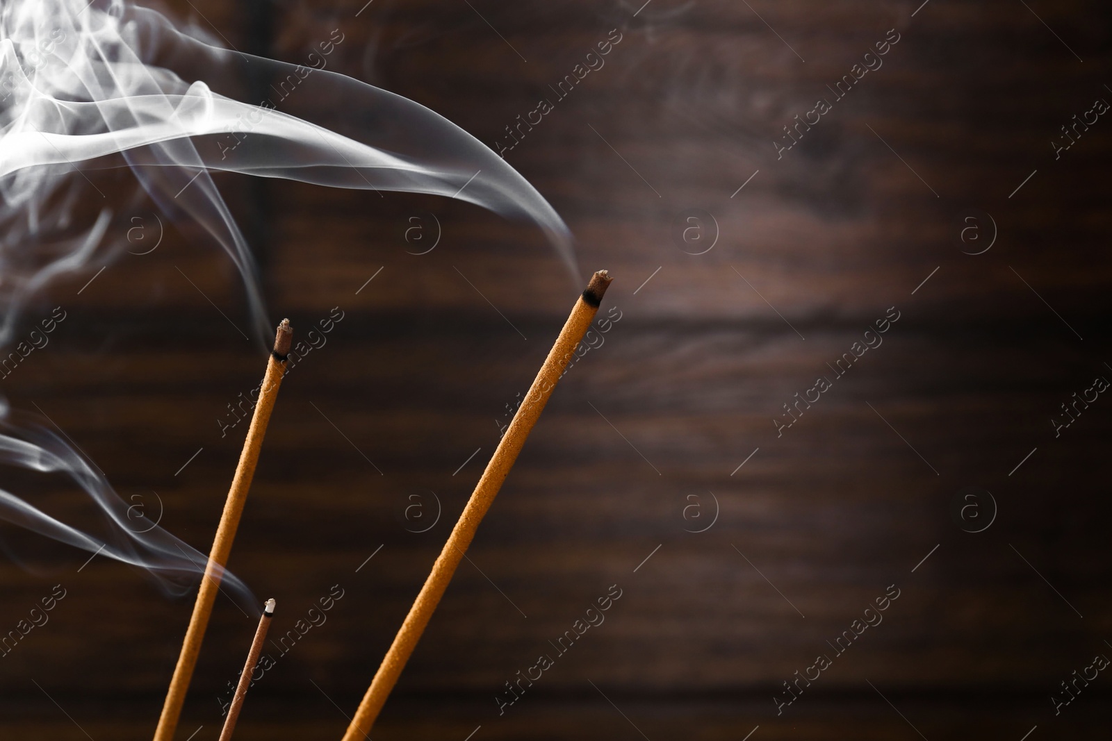 Photo of Aromatic incense sticks smoldering on blurred background, closeup. Space for text