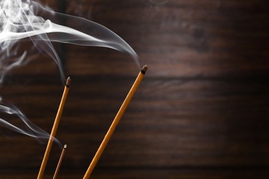 Aromatic incense sticks smoldering on blurred background, closeup. Space for text