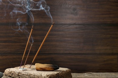 Photo of Aromatic incense sticks smoldering on wooden table. Space for text