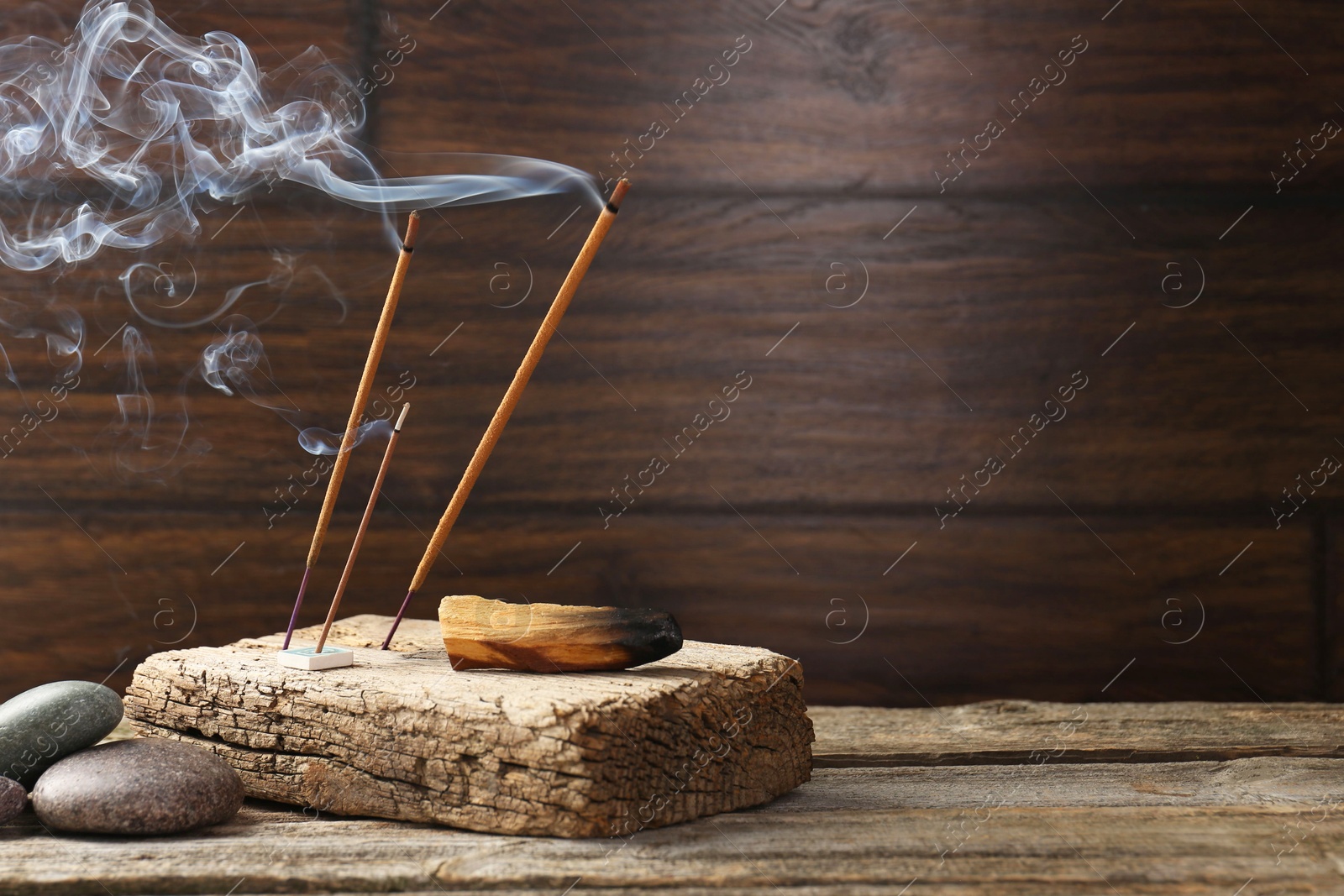 Photo of Aromatic incense sticks smoldering on wooden table. Space for text