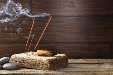 Photo of Aromatic incense sticks smoldering on wooden table. Space for text