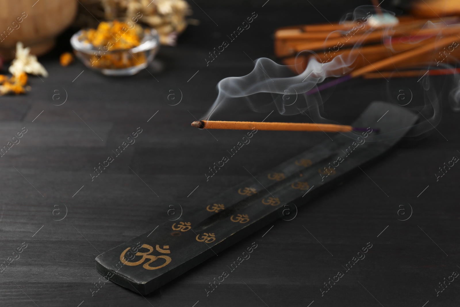 Photo of Aromatic incense stick smoldering in holder with om sign on black table