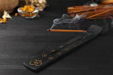 Aromatic incense stick smoldering in holder with om sign on black table