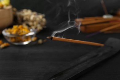 Photo of Aromatic incense stick smoldering in holder with om sign on black table, closeup