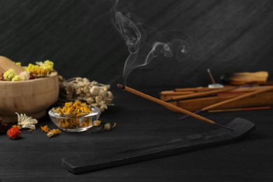 Photo of Aromatic incense stick smoldering in holder with om sign on black table