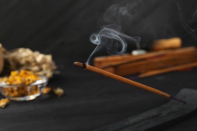 Aromatic incense stick smoldering on blurred background, closeup