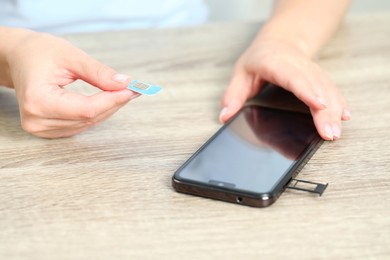 Woman holding SIM card near smartphone at wooden, closeup