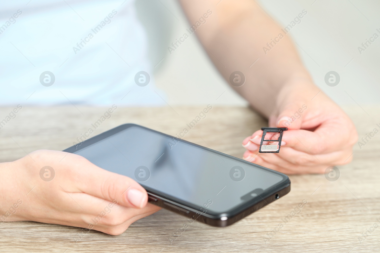 Photo of Woman holding slot tray with SIM card and smartphone at wooden table indoors, closeup