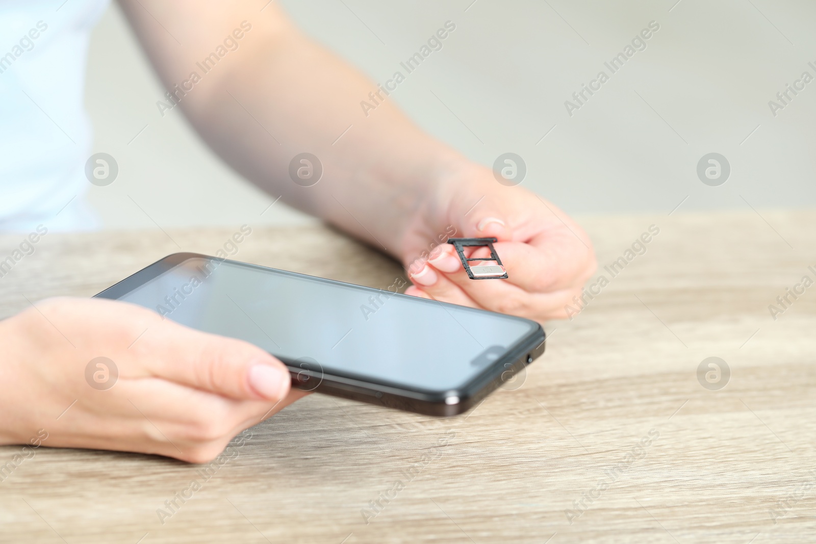 Photo of Woman holding slot tray with SIM card and smartphone at wooden table indoors, closeup