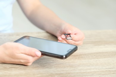 Photo of Woman holding slot tray with SIM card and smartphone at wooden table indoors, closeup