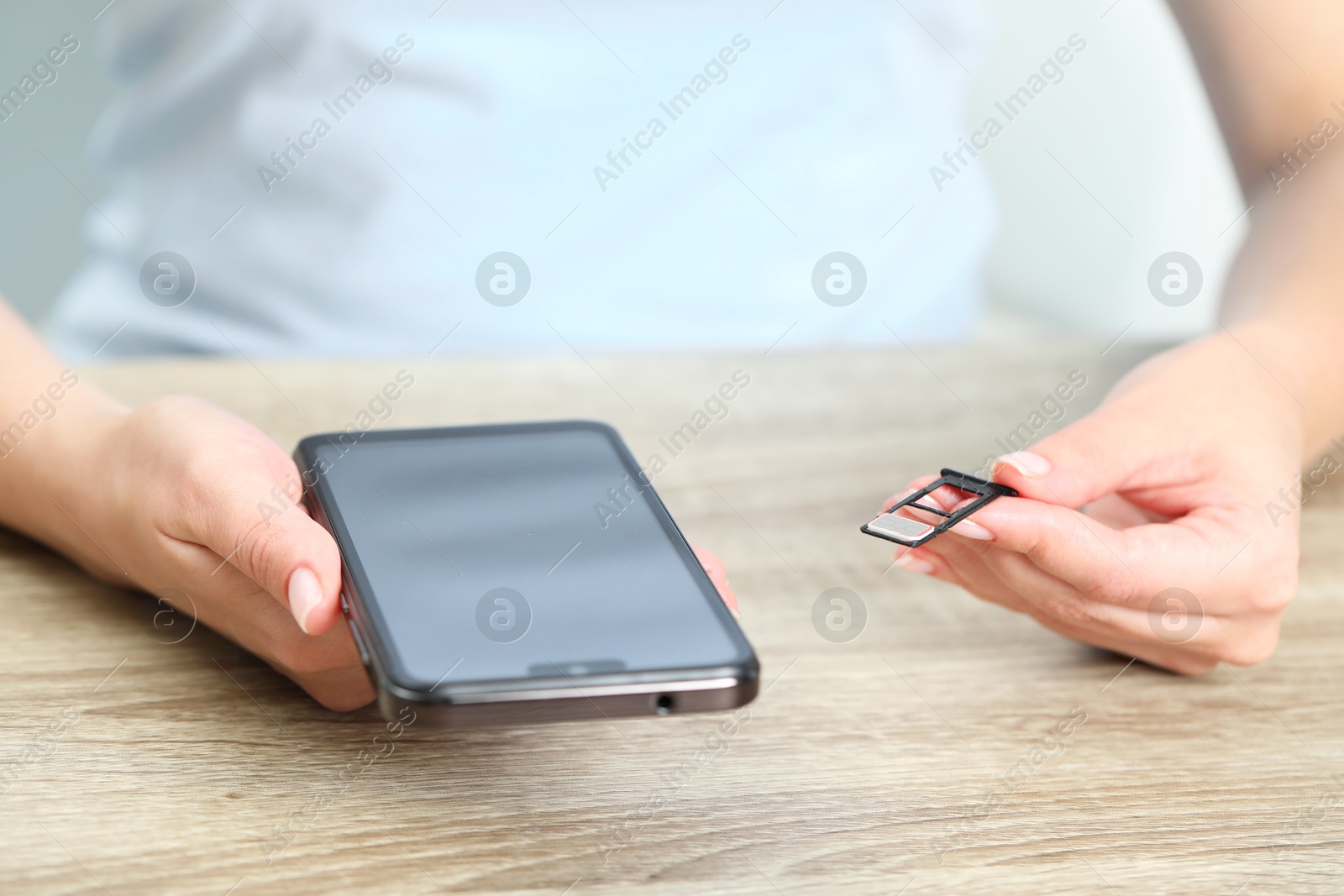 Photo of Woman holding slot tray with SIM card and smartphone at wooden table indoors, closeup