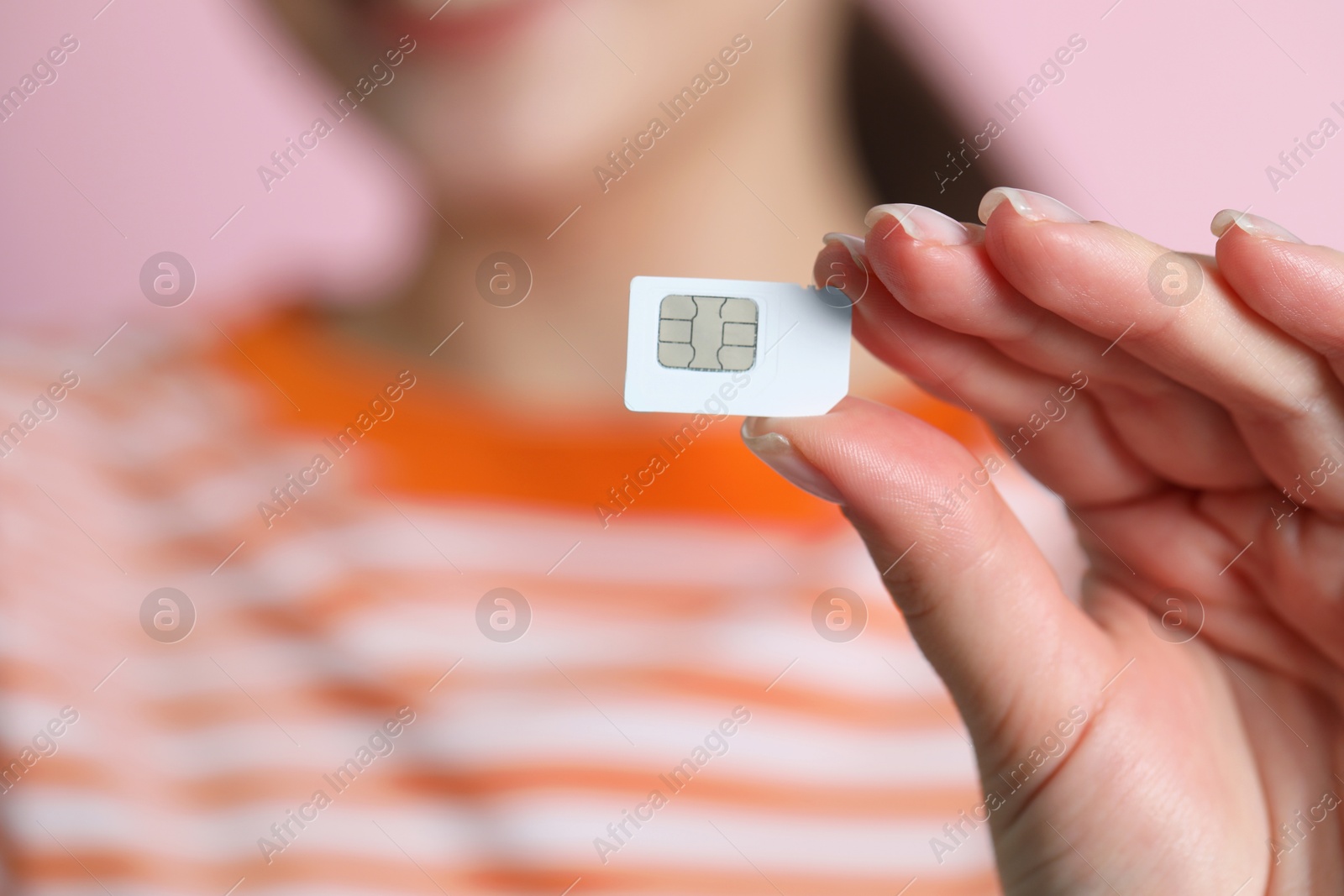 Photo of Woman holding SIM card on pink background, closeup