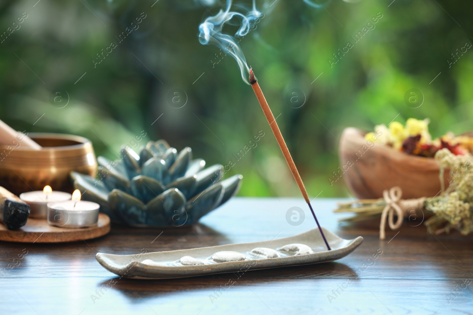 Photo of Incense stick smoldering in holder and burning candles on wooden table outdoors