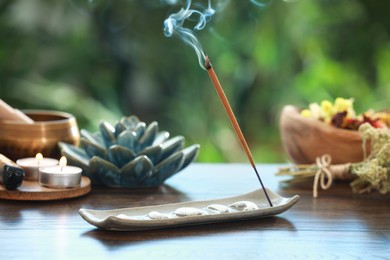 Incense stick smoldering in holder and burning candles on wooden table outdoors