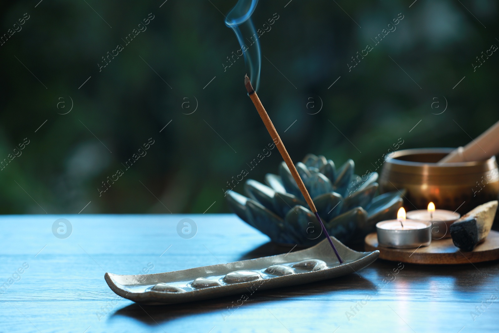 Photo of Incense stick smoldering in holder and burning candles on wooden table outdoors