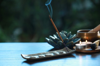 Incense stick smoldering in holder and burning candles on wooden table outdoors