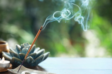 Photo of Incense stick smoldering in holder and burning candle on table outdoors, space for text