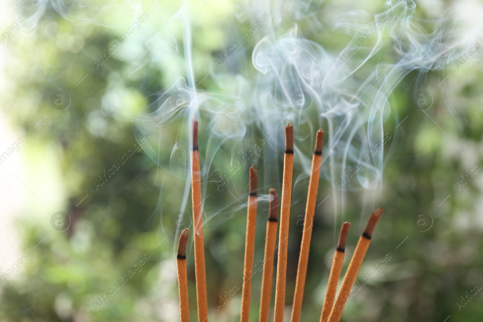 Photo of Incense sticks smoldering on green blurred background, space for text