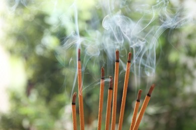 Photo of Incense sticks smoldering on green blurred background, space for text