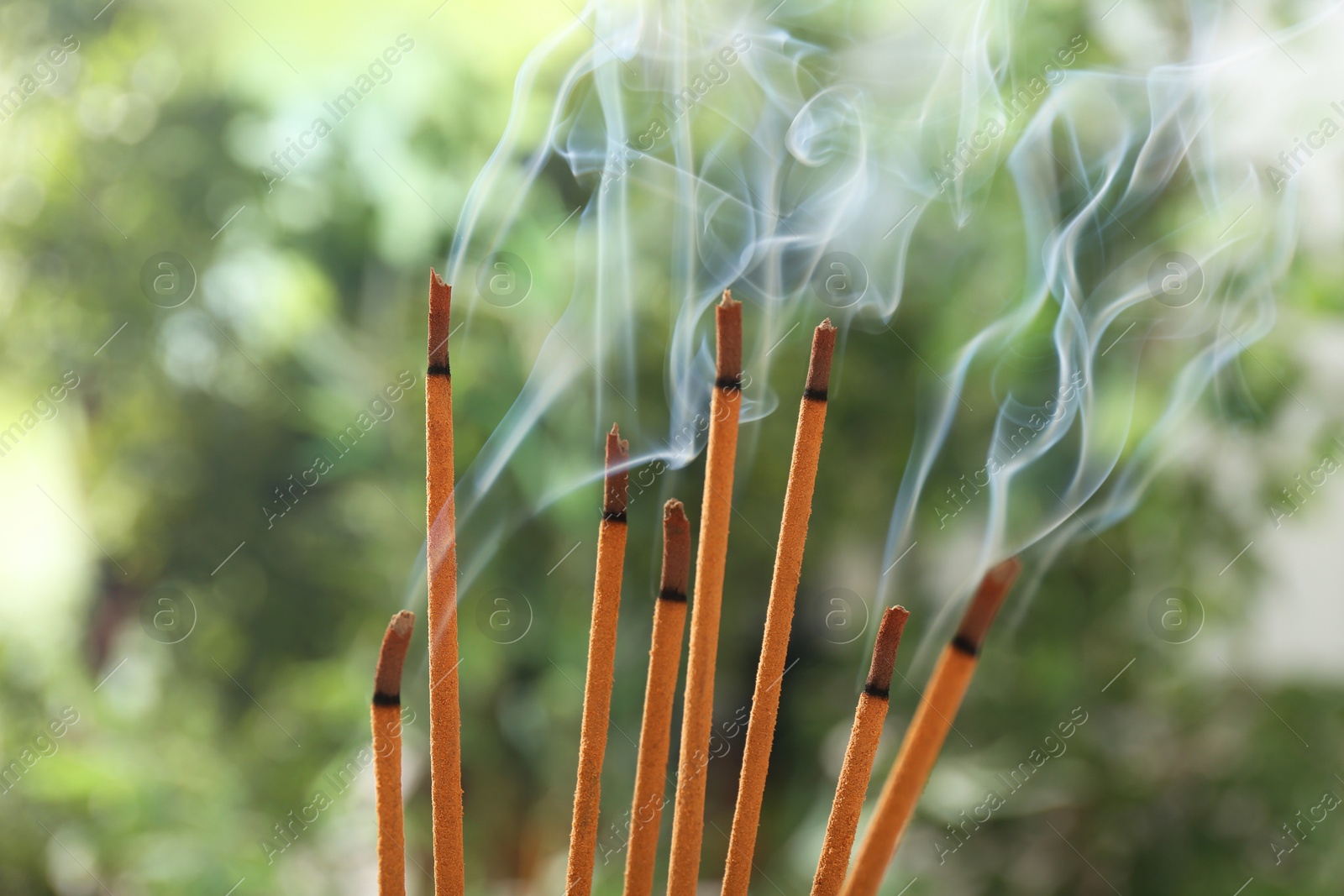 Photo of Incense sticks smoldering on green blurred background