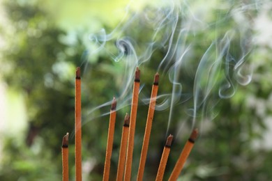 Photo of Incense sticks smoldering on green blurred background