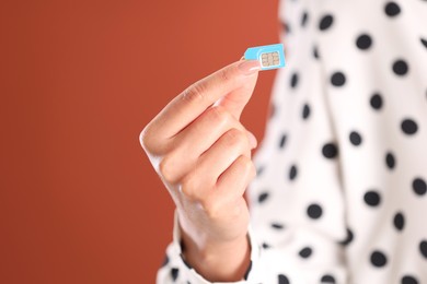 Photo of Woman holding SIM card on terracotta background, closeup