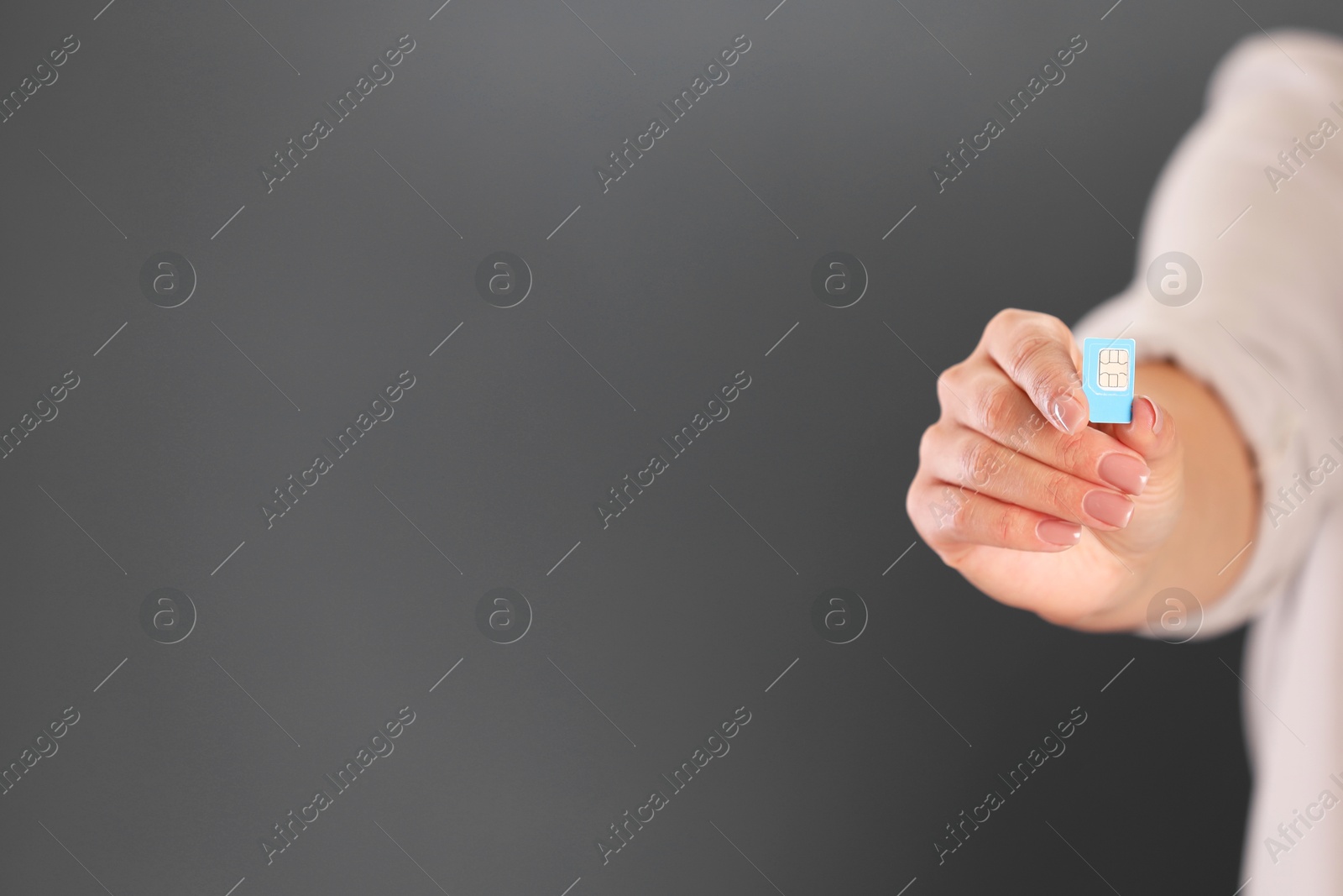 Photo of Woman holding SIM card on dark grey background, closeup. Space for text