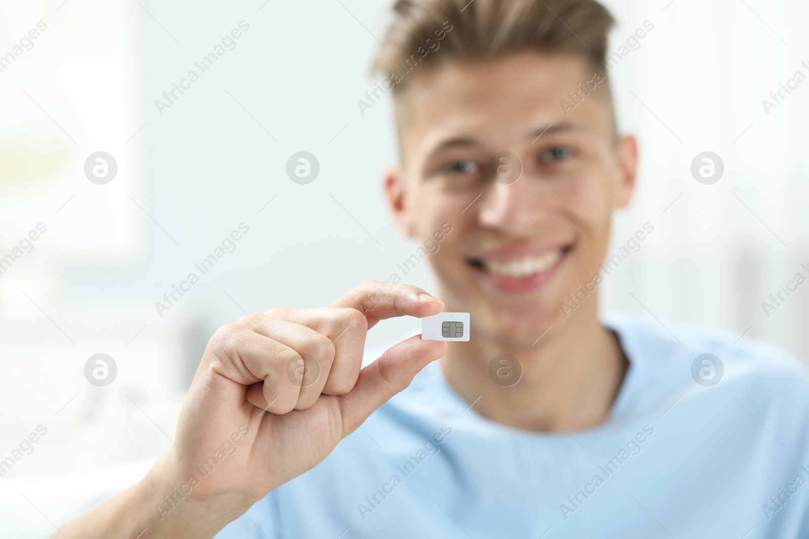 Photo of Happy man with SIM card indoors, selective focus