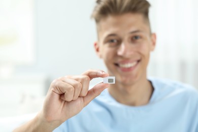 Happy man with SIM card indoors, selective focus