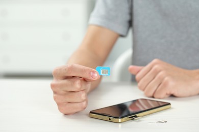 Man with SIM card near smartphone at white wooden table indoors, closeup