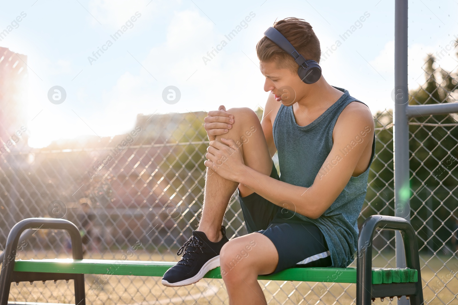 Photo of Sportsman with leg injury suffering from knee pain on bench at stadium, space for text