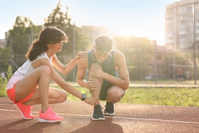 Photo of Sports injury. Woman helping man with leg pain at stadium, space for text