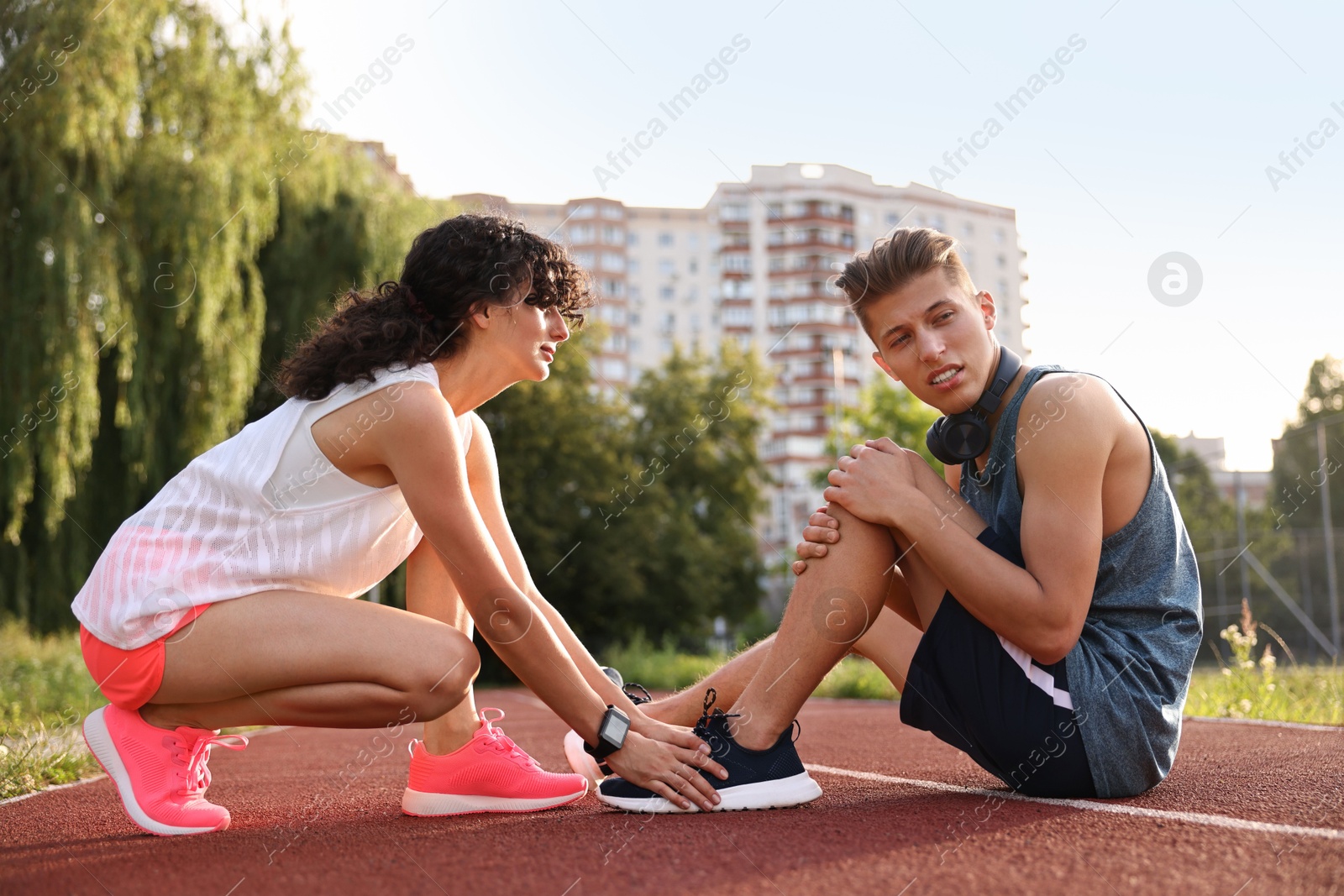 Photo of Sports injury. Woman helping man with leg pain at stadium