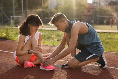 Sports injury. Man helping woman with leg pain at stadium