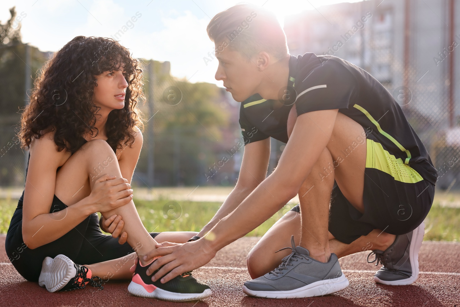 Photo of Sports injury. Man helping woman with leg pain at stadium