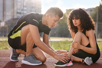 Photo of Sports injury. Man helping woman with leg pain at stadium