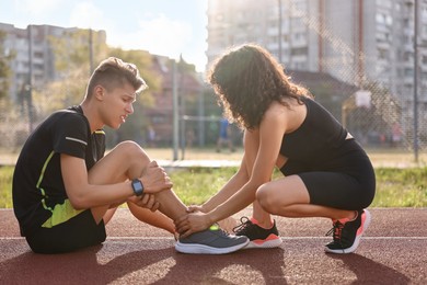 Sports injury. Woman helping man with leg pain at stadium