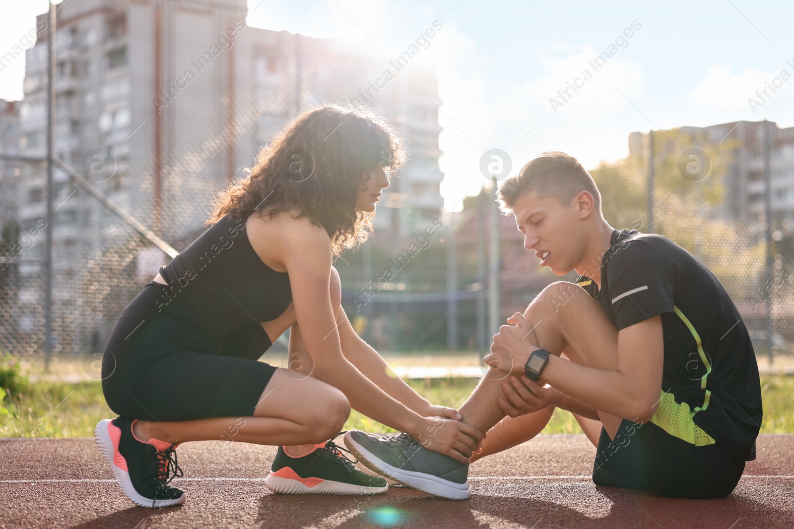 Photo of Sports injury. Woman helping man with leg pain at stadium