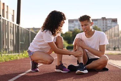 Photo of Sports injury. Woman helping man with knee pain at stadium