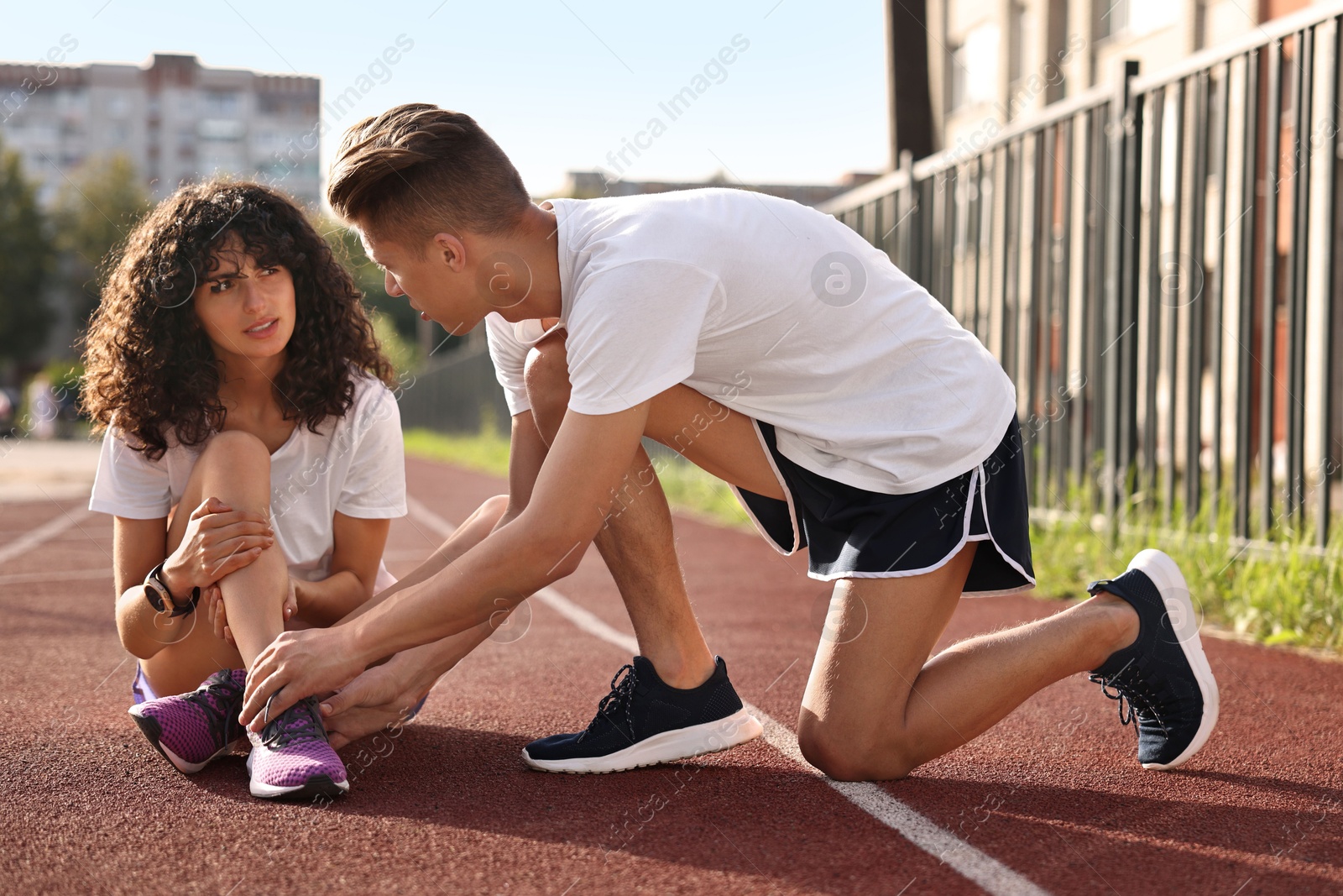 Photo of Sports injury. Man helping woman with leg pain at stadium