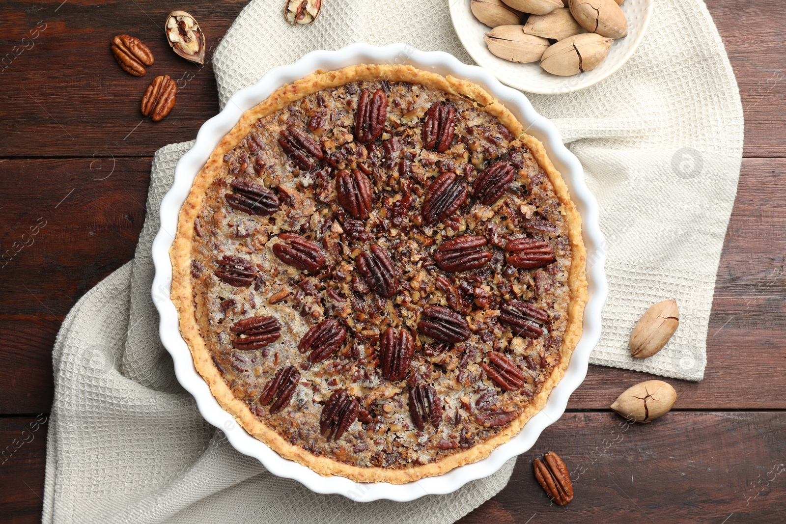 Photo of Delicious pecan pie in baking dish and fresh nuts on wooden table, flat lay