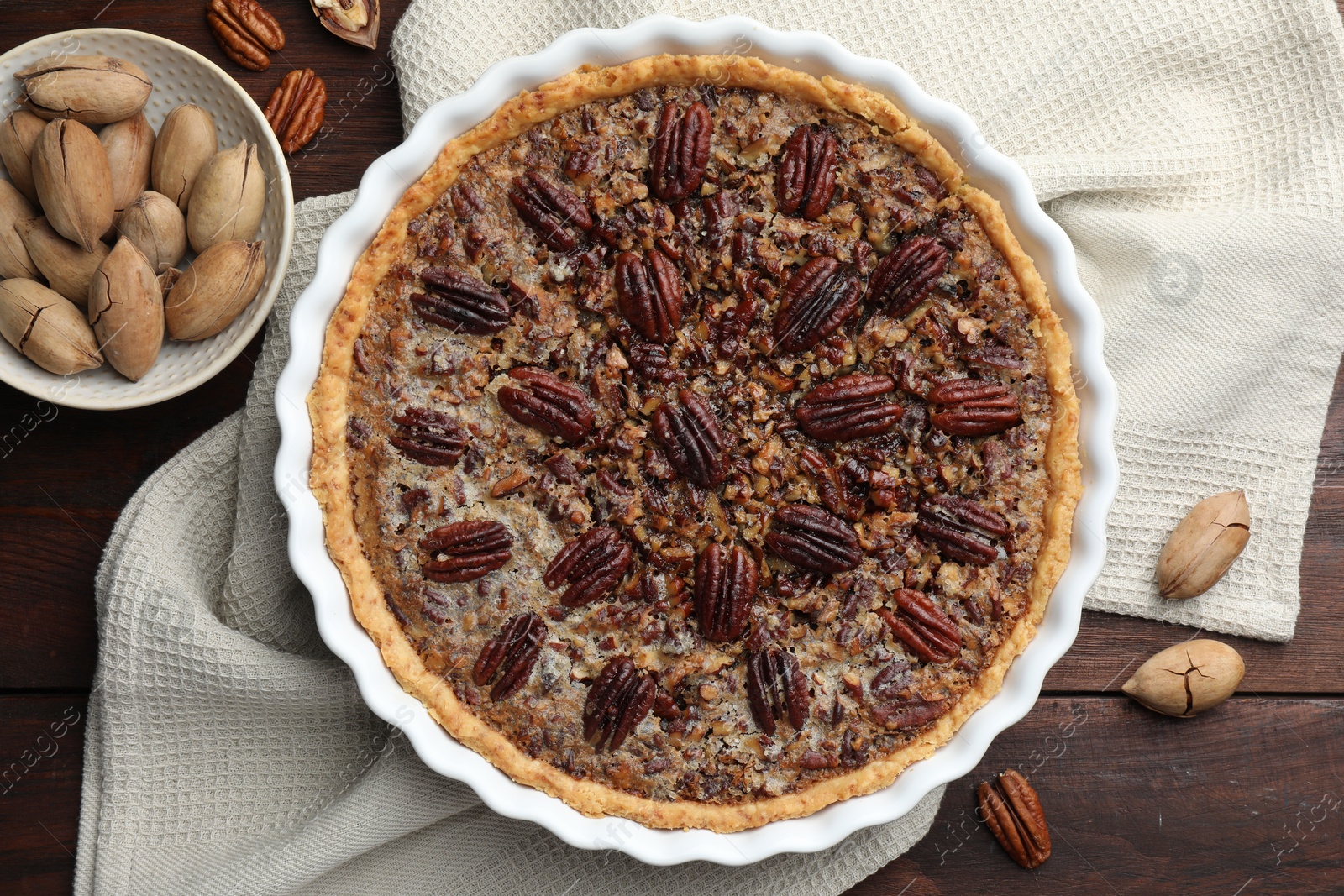 Photo of Delicious pecan pie in baking dish and fresh nuts on wooden table, flat lay