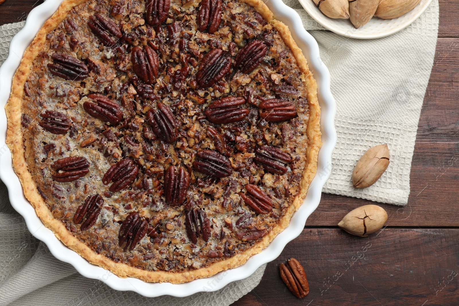 Photo of Delicious pecan pie in baking dish and fresh nuts on wooden table, flat lay