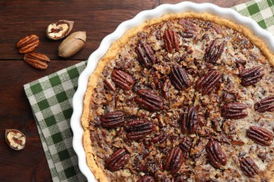 Delicious pecan pie in baking dish and fresh nuts on wooden table, top view